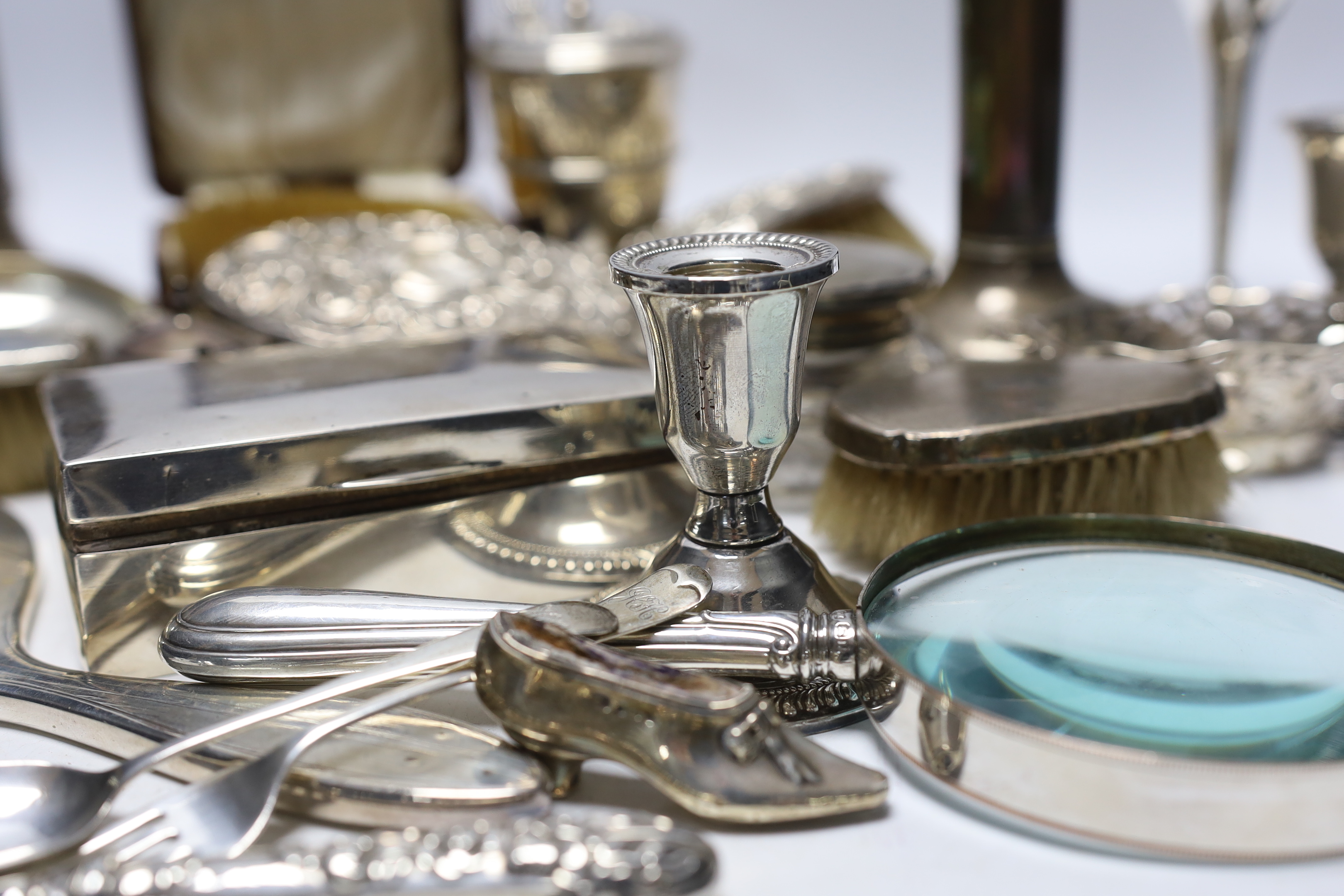 Sundry silver items including a pair of candlesticks, marks rubbed, handled magnifying glass, lidded vase, hand mirror, five brushes, cigarette box, trinket box, toilet jar and eleven other items including a novelty shoe